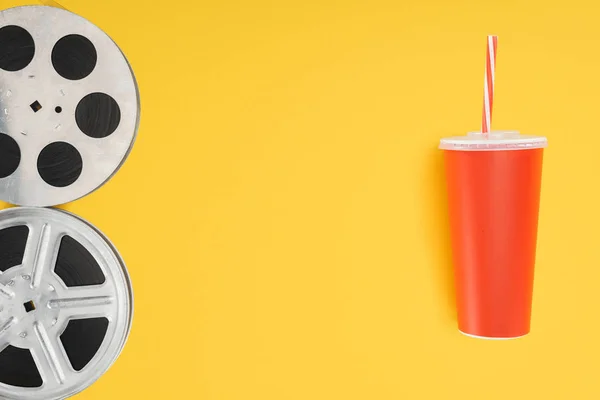 Film reels and red disposable cup with straw isolated on yellow — Stock Photo