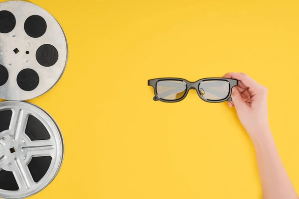 Film reels and female hand holding stereoscopic 3d glasses isolated on yellow — Stock Photo