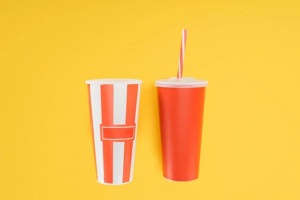 Смугасте попкорнове відро і червона одноразова чашка з соломою ізольовані на жовтому — стокове фото