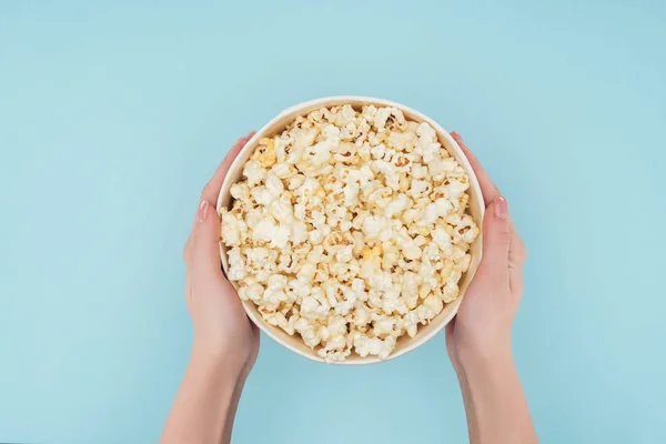 Vista dall'alto di mani che tengono secchio con popcorn isolato su blu — Foto stock