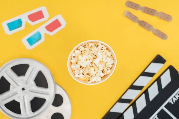 Vista dall'alto di clapperboard, bobine di film, occhiali 3d, biglietti per il cinema e popcorn secchio isolato su giallo — Foto stock