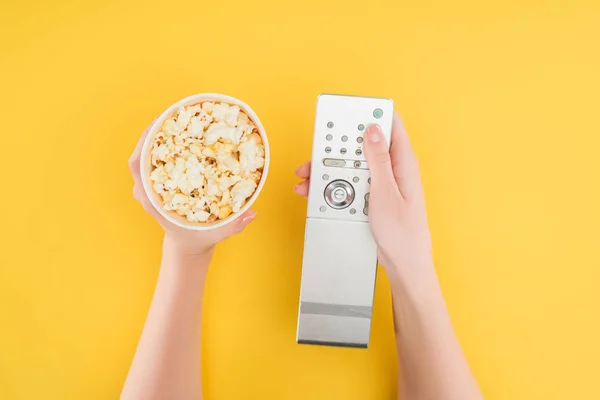 Top view of hands holding popcorn bucket and remote controller isolated on yellow — Stock Photo