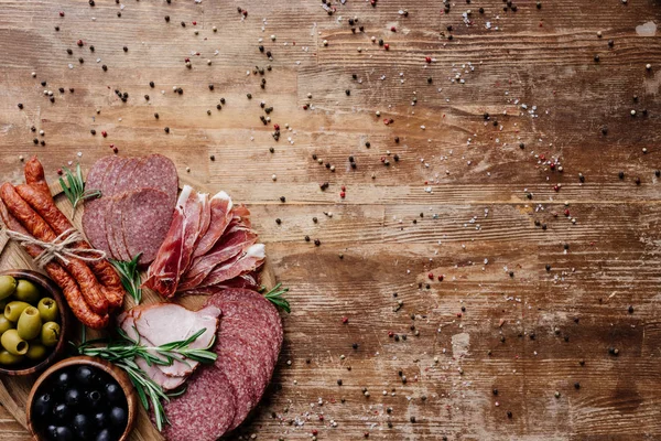 Top view of round cutting board with tasty salami, smoked sausages and olives on wooden table with scattered spices — Stock Photo