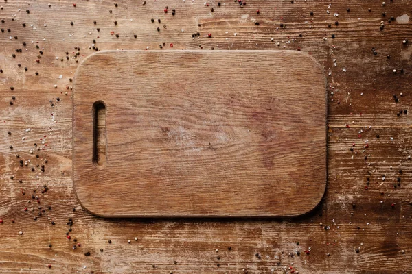 Vue du dessus de la planche à découper sur une table en bois avec des grains de poivre épars — Photo de stock