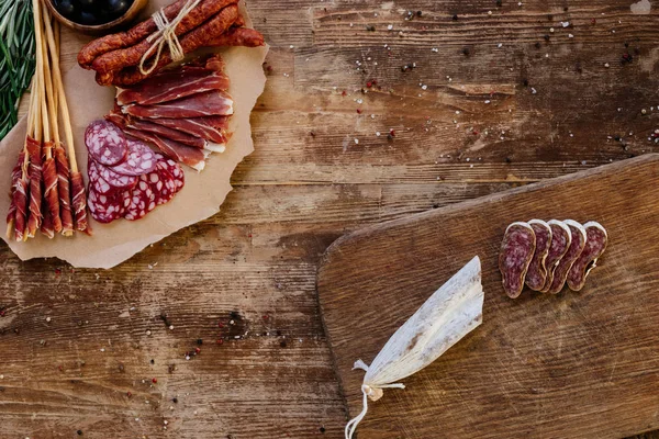 Top view of cutting boards with sliced prosciutto, salami and smoked sausages on wooden table  with scattered spices — Stock Photo