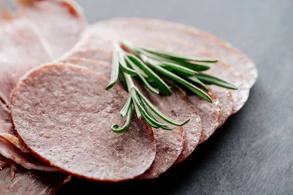 Close up view of little rosemary branch on delicious sliced salami — Stock Photo