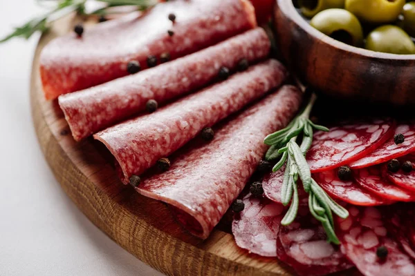 Close up view of delicious sliced salami with rosemary and peppercorns on wooden cutting board — Stock Photo