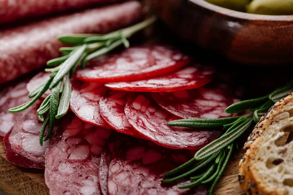 Close up view of delicious sliced salami with rosemary and bread on wooden cutting board — Stock Photo