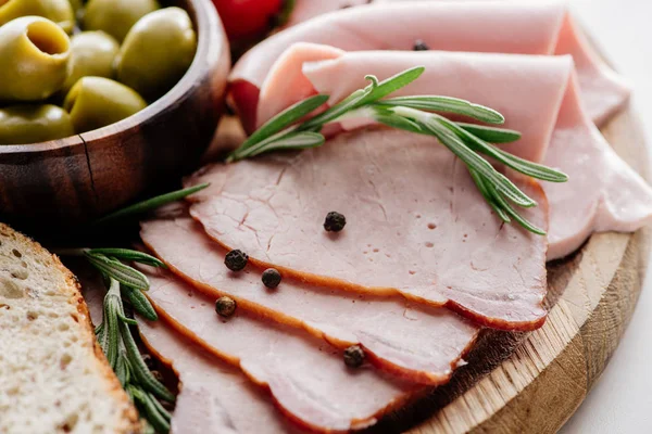 Close up view of olives in bowl and delicious sliced ham with spices and herbs on wooden cutting board — Stock Photo