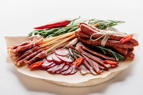 Tábua de corte redonda com pimenta, ervas e salame delicioso, presunto e salsichas defumadas em papel de embrulho marrom — Fotografia de Stock