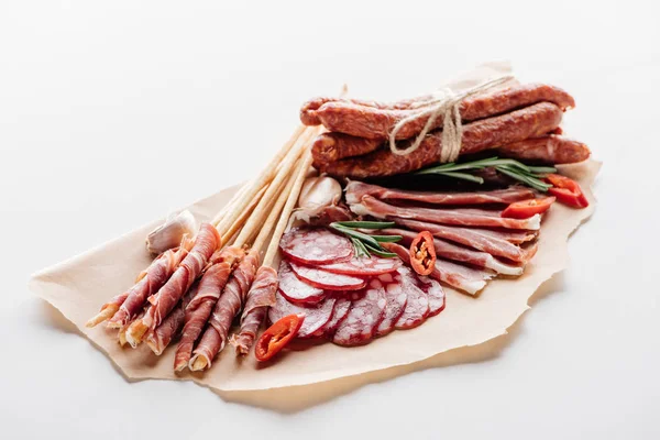 Papier d'emballage marron avec délicieux salami, saucisses fumées et herbes sur table blanche — Photo de stock