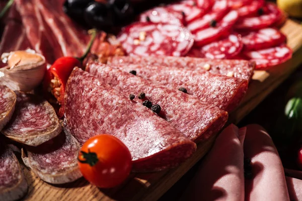 Close up view of sliced salami with tomato, peppercorns and chili on wooden cutting board — Stock Photo