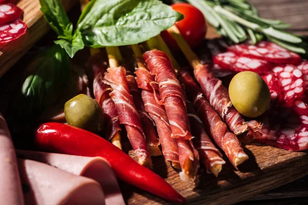 Close up view of sliced salami, ham and prosciutto with vegetables and herbs on wooden cutting board — Stock Photo