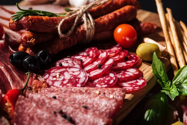 Close up view of delicious smoked sausages and sliced salami with vegetables on wooden cutting board — Stock Photo