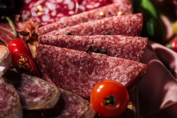 Close up view of tasty sliced salami with vegetables and spices on wooden cutting board — Stock Photo