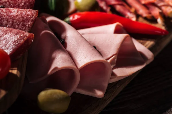 Close up view of wooden cutting board with tasty sliced ham and vegetables — Stock Photo