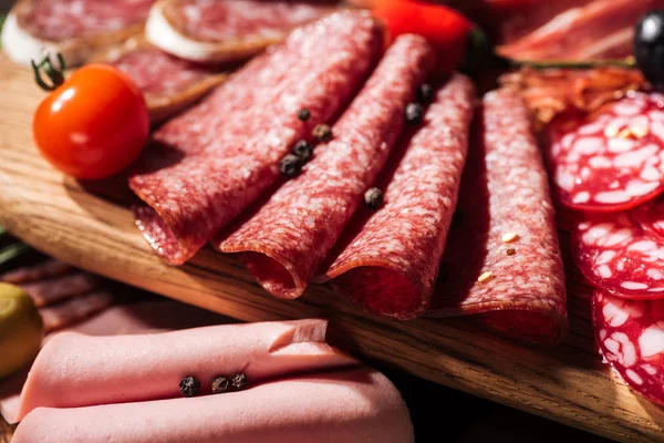 Close up view of wooden cutting board with delicious sliced salami, spices and vegetables — Stock Photo