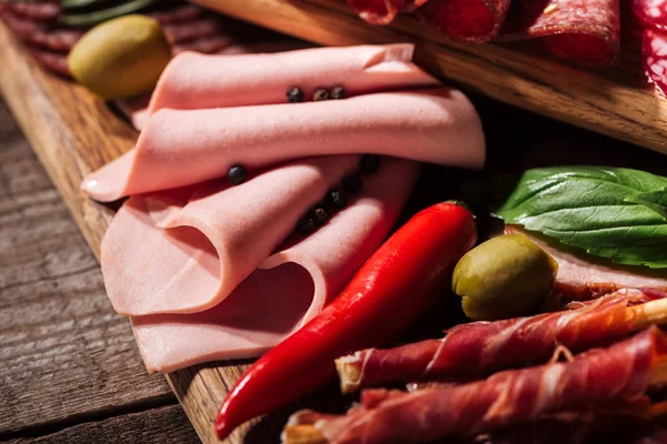 Close up view of wooden cutting board with delicious sliced ham and prosciutto — Stock Photo