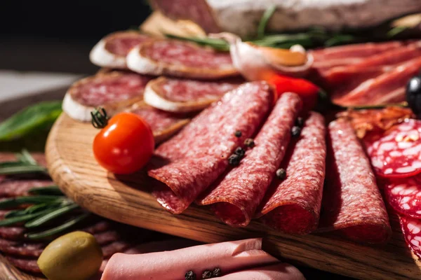Close up view of wooden cutting board with delicious sliced salami and vegetables — Stock Photo