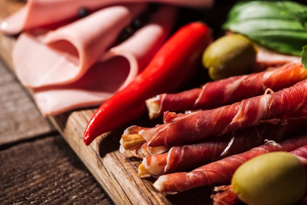 Close up view of wooden cutting boards with chili, olives, delicious sliced salami and prosciutto — Stock Photo