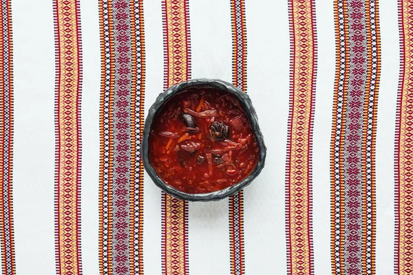 Top view of traditional tasty beetroot soup with embroidered towel on background — Stock Photo