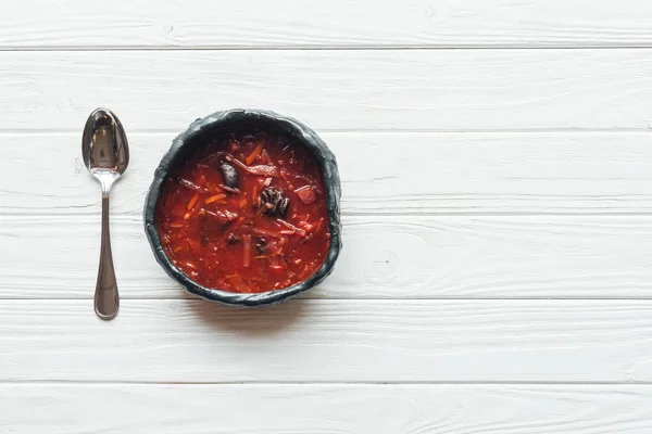 Top view of traditional tasty beetroot soup with spoon on white wooden background with copy space — Stock Photo