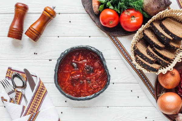 Draufsicht auf köstliche traditionelle Rote-Bete-Suppe mit Zutaten und Besteck auf weißem Holzgrund — Stockfoto