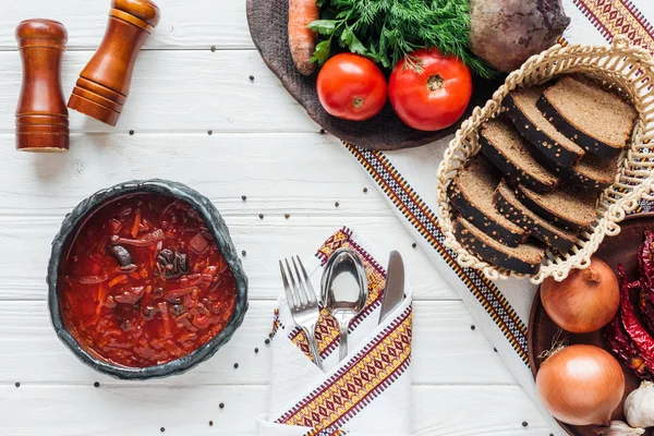 Ansicht der traditionellen Rote-Bete-Suppe mit Zutaten und Besteck auf weißem Holzgrund — Stockfoto
