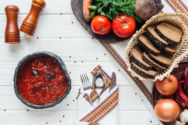 Top view of traditional beetroot soup with ingredients and cutlery on white wooden background — Stock Photo