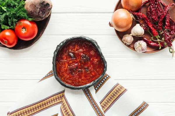 Traditional beetroot soup with ingredients and embroidered towel on white wooden background — Stock Photo