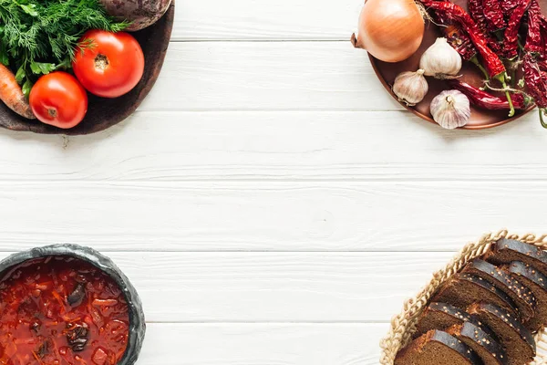 Vista dall'alto della tradizionale zuppa di barbabietole con ingredienti vegetali e pane nero su sfondo bianco in legno con spazio copia — Foto stock