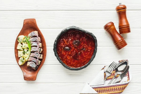 Top view of traditional beetroot soup with herring and cutlery on white wooden background — Stock Photo