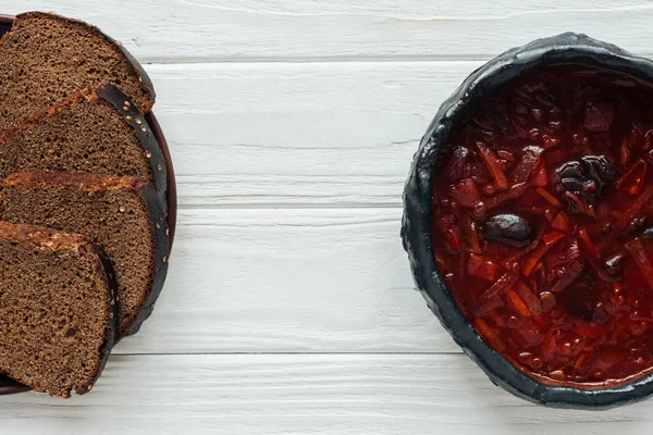 Schüssel mit köstlicher traditioneller Rote-Bete-Suppe mit Roggenbrot auf weißem Holzgrund — Stockfoto