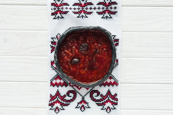 Schüssel mit leckerer traditioneller Rote-Bete-Suppe mit besticktem Handtuch auf weißem Holzhintergrund — Stockfoto