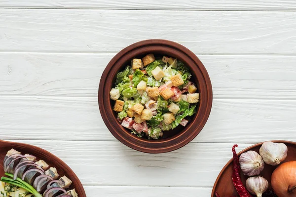 Top view of delicious traditional caesar salad with croutons and dishes around on white wooden background — Stock Photo