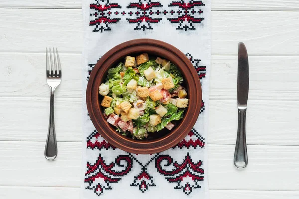 Blick von oben auf köstlichen traditionellen Caesar-Salat mit Croutons, Besteck und besticktem Handtuch auf weißem Holzhintergrund — Stockfoto