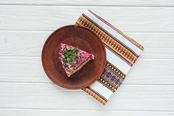 Vue de dessus de savoureuse salade russe traditionnelle sur assiette avec serviette brodée sur fond blanc en bois — Photo de stock