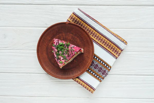 Top view of tasty traditional russian salad on plate with embroidered towel on white wooden background — Stock Photo