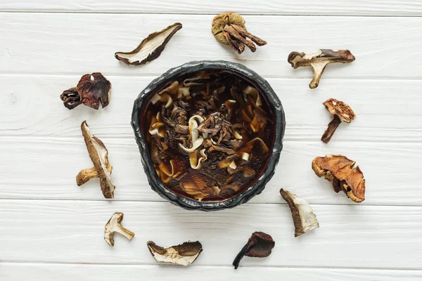 Vista superior de sopa de cogumelos tradicional saborosa com círculo de cogumelos secados no fundo de madeira branco — Fotografia de Stock
