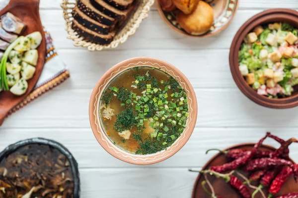 Селективный фокус традиционного рыбного супа с зеленым луком и блюдами на белом деревянном фоне — стоковое фото