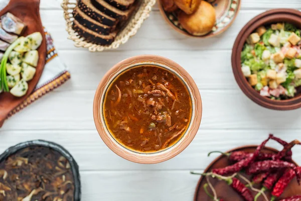 Messa a fuoco selettiva di deliziosa zuppa di carne mista tradizionale e piatti intorno su sfondo di legno bianco — Foto stock