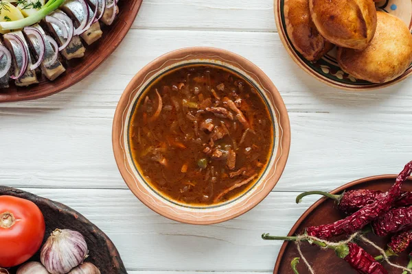 Vista dall'alto di gustosa zuppa di carne mista tradizionale e piatti intorno su sfondo di legno bianco — Foto stock