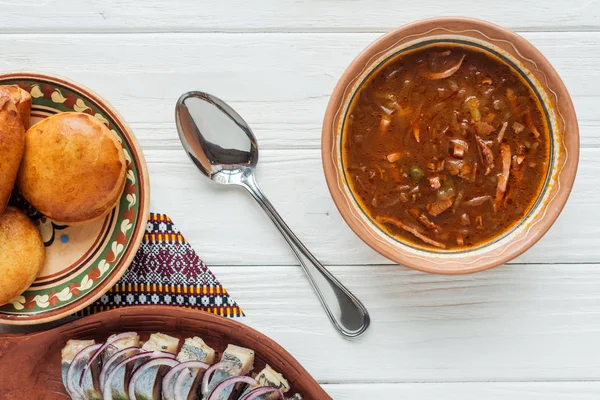 Vista superior de la sabrosa sopa de carne mixta tradicional con mini pasteles y cuchara sobre fondo de madera blanca - foto de stock