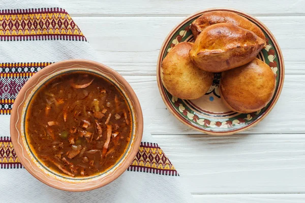 Deliciosa sopa tradicional de carne mista com mini tortas e toalha bordada no fundo de madeira branca — Fotografia de Stock