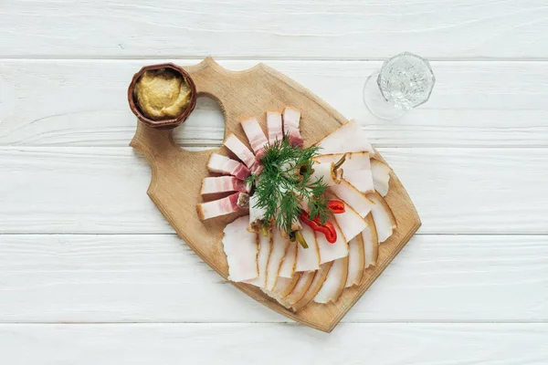 Draufsicht auf traditionell geschnittenes Räucherschmalz auf Schneidebrett mit Senf und Wodka auf weißem Holzhintergrund — Stockfoto