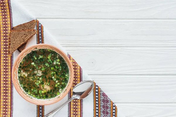 Traditional fish soup with green onion, embroidered towel, spoon and rye bread on white wooden background — Stock Photo