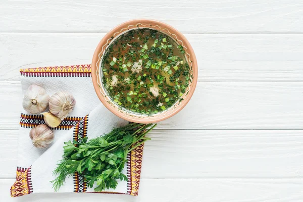 Top view of traditional fish soup with green onion, embroidered towel and greens on white wooden background — Stock Photo