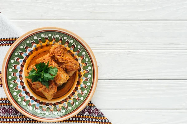 Delicious stuffed cabbage rolls with parsley, embroidered towel and copy space on white wooden background — Stock Photo