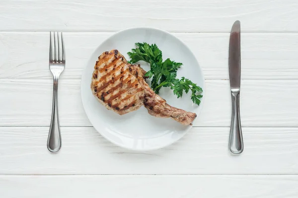 Vista superior de bife de carne saborosa costela olho na placa com salsa e talheres em fundo de madeira branca — Fotografia de Stock