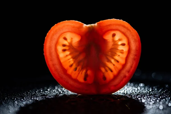 Rebanada de tomate fresco con retroiluminación sobre fondo negro - foto de stock